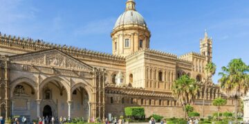 Esterno della Cattedrale di Palermo in una giornata di sole, con facciata storica, cupola e palme in primo piano.