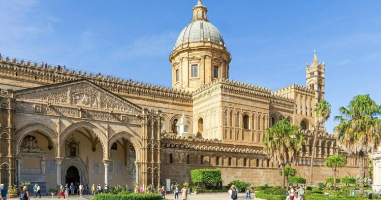 Esterno della Cattedrale di Palermo in una giornata di sole, con facciata storica, cupola e palme in primo piano.